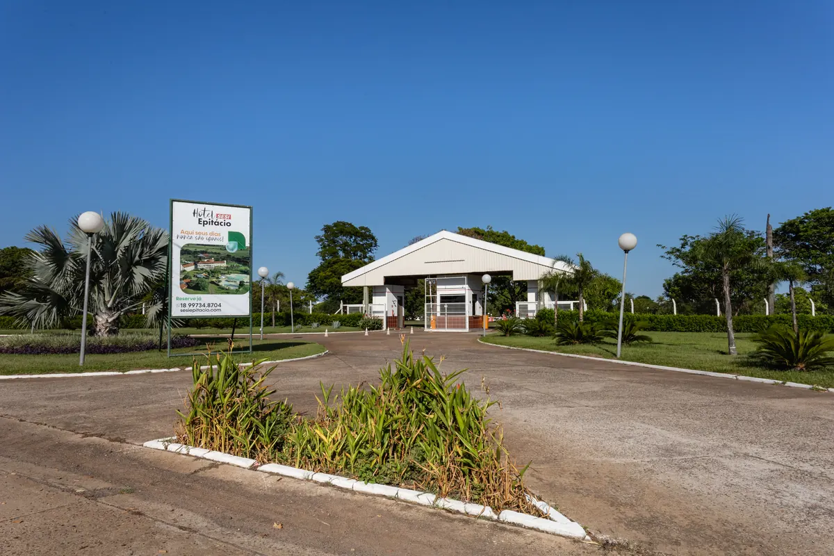 Portaria de entrada do hotel com placa de boas-vindas, alameda e jardins.