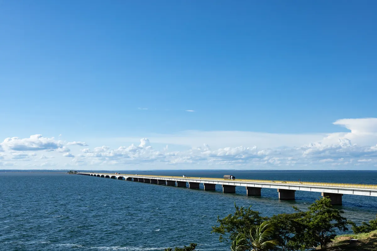 Rio Paraná de águas azuis com a longa ponte ao fundo e céu com nuvens.