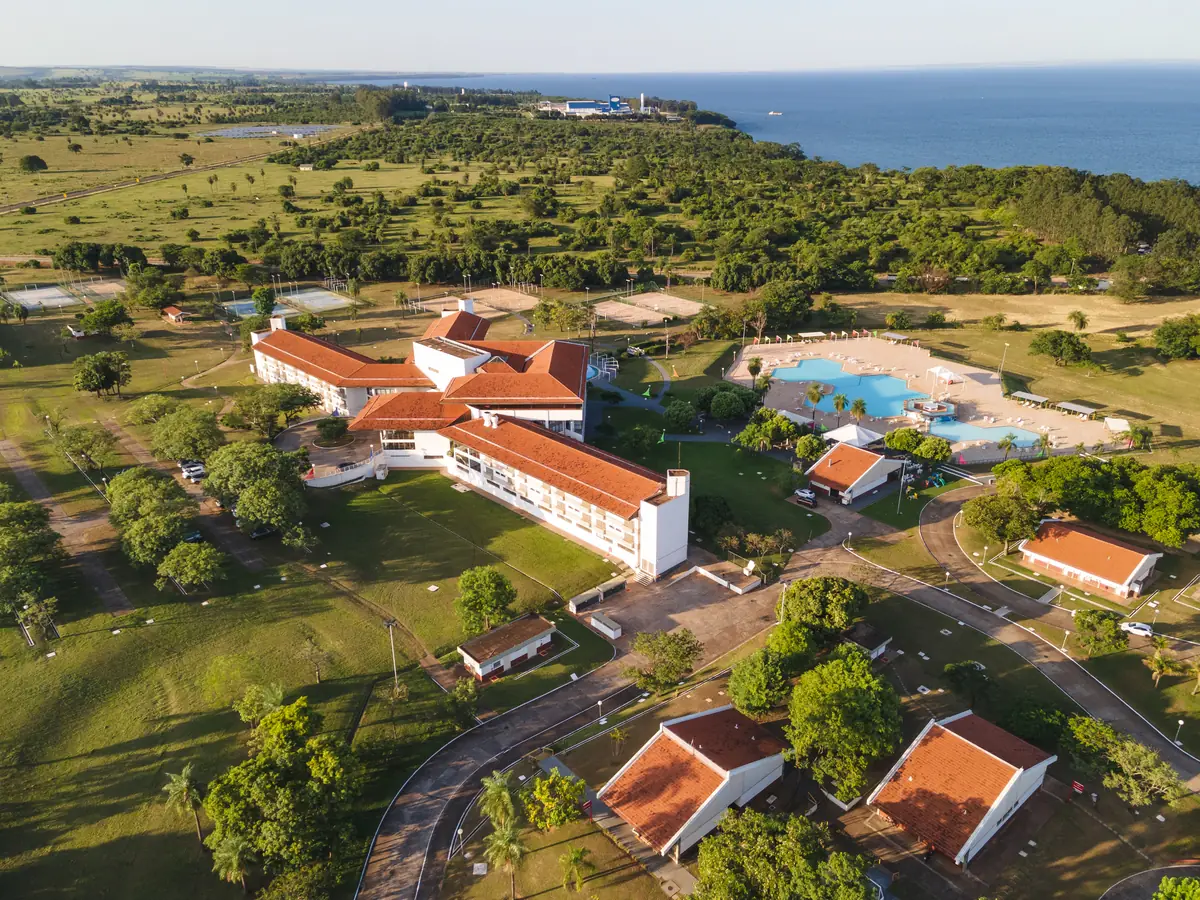 Vista aérea ampla do hotel, chalés com telhado vermelho, piscinas e rio