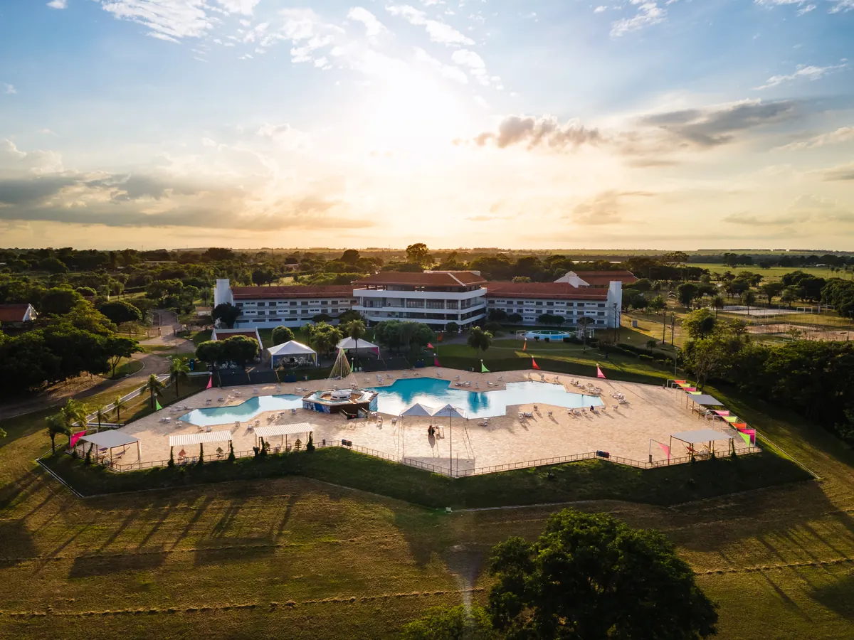 Vista aérea do complexo de piscinas em forma de estrela com os prédios do hotel ao fundo, ao entardecer