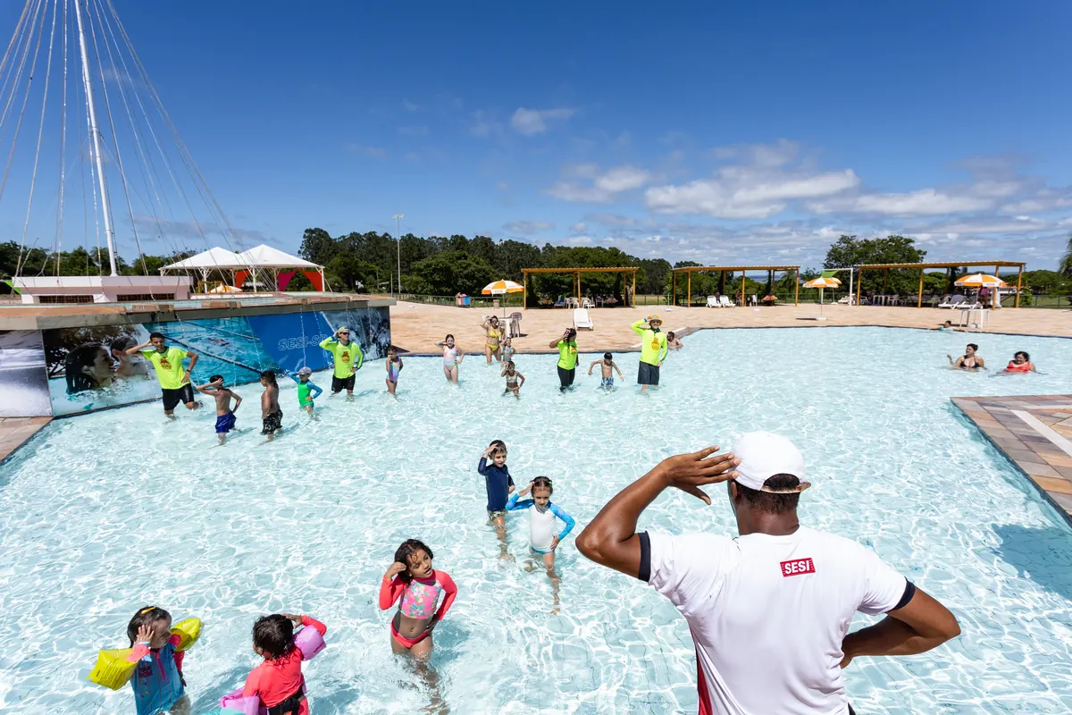 Monitor de costas diante da piscina com crianças e equipe de recreação, céu azul