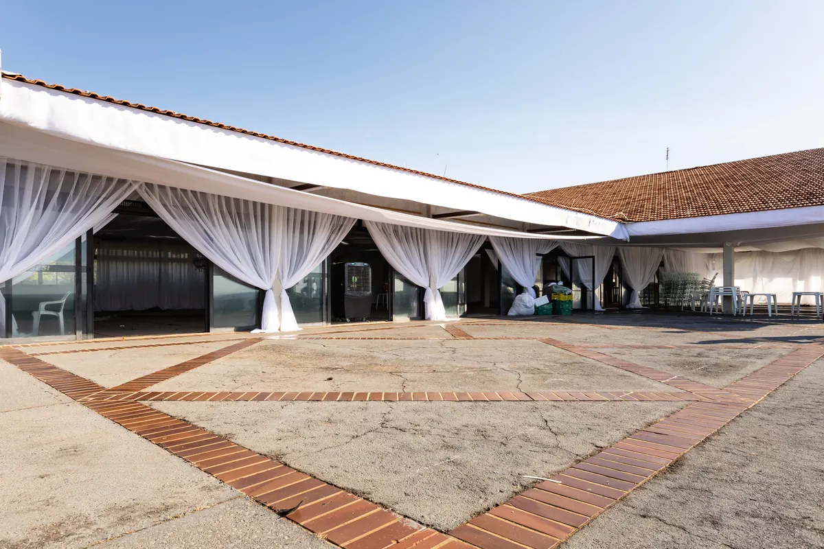 Fachada do salão de eventos com cortinas brancas amarradas e pátio de piso de tijolos