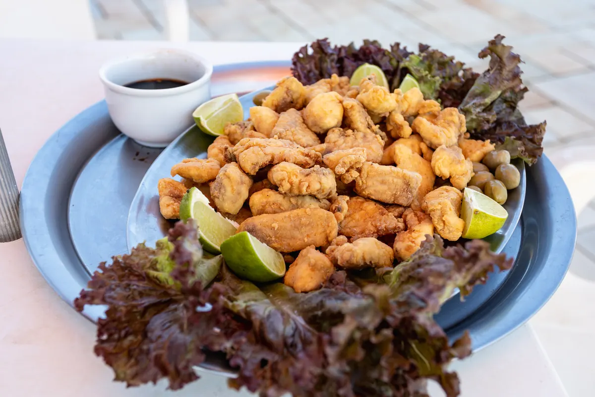 Porção de peixe frito com limão e alface roxa servida à beira da piscina