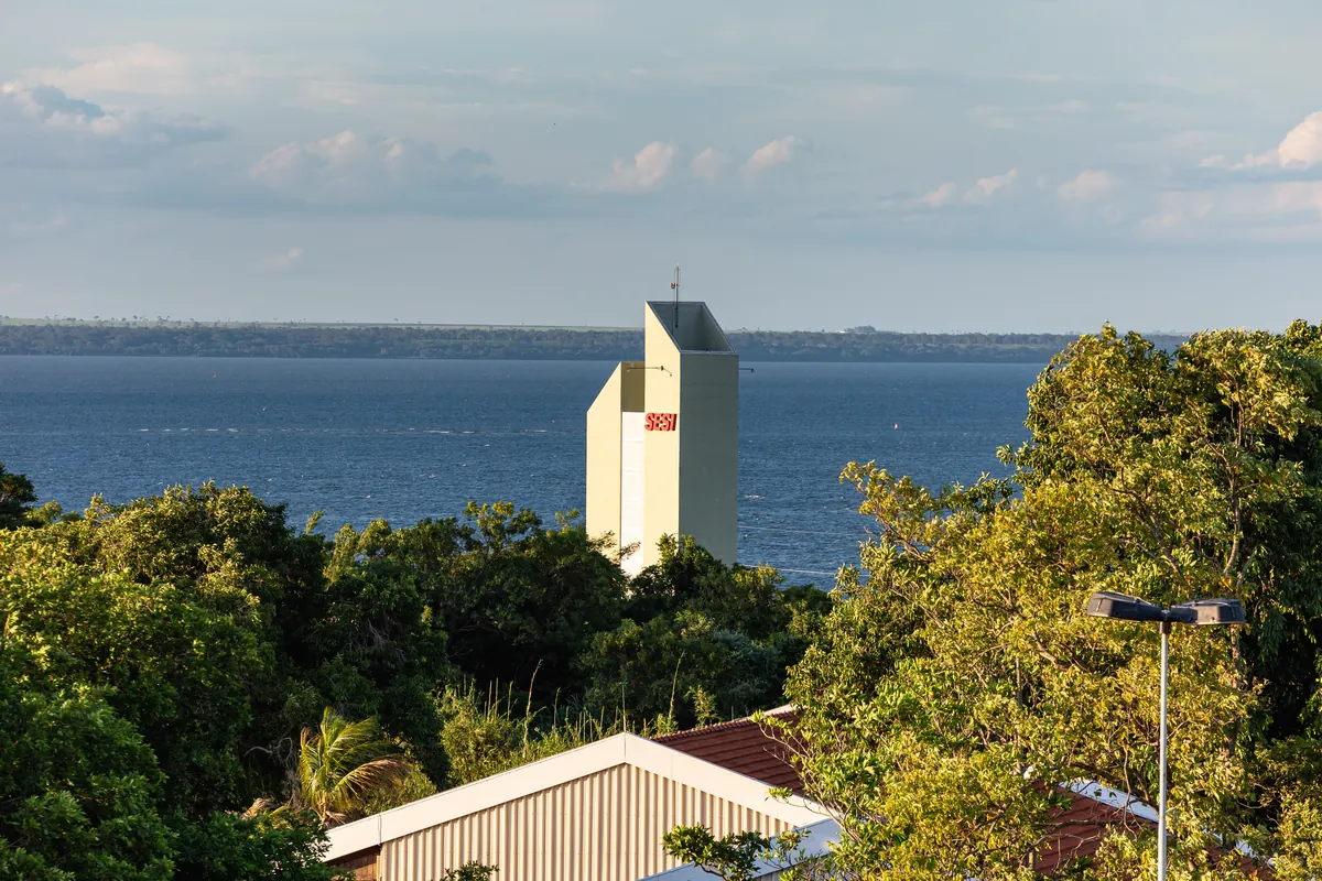 Torre/caixa d'água com logo SESI entre árvores, com o rio Paraná ao fundo