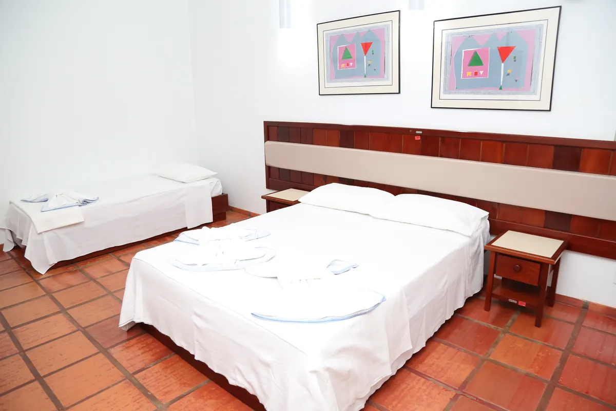 Apartamento com cama de casal, cama de solteiro, criado-mudo e quadros na parede
