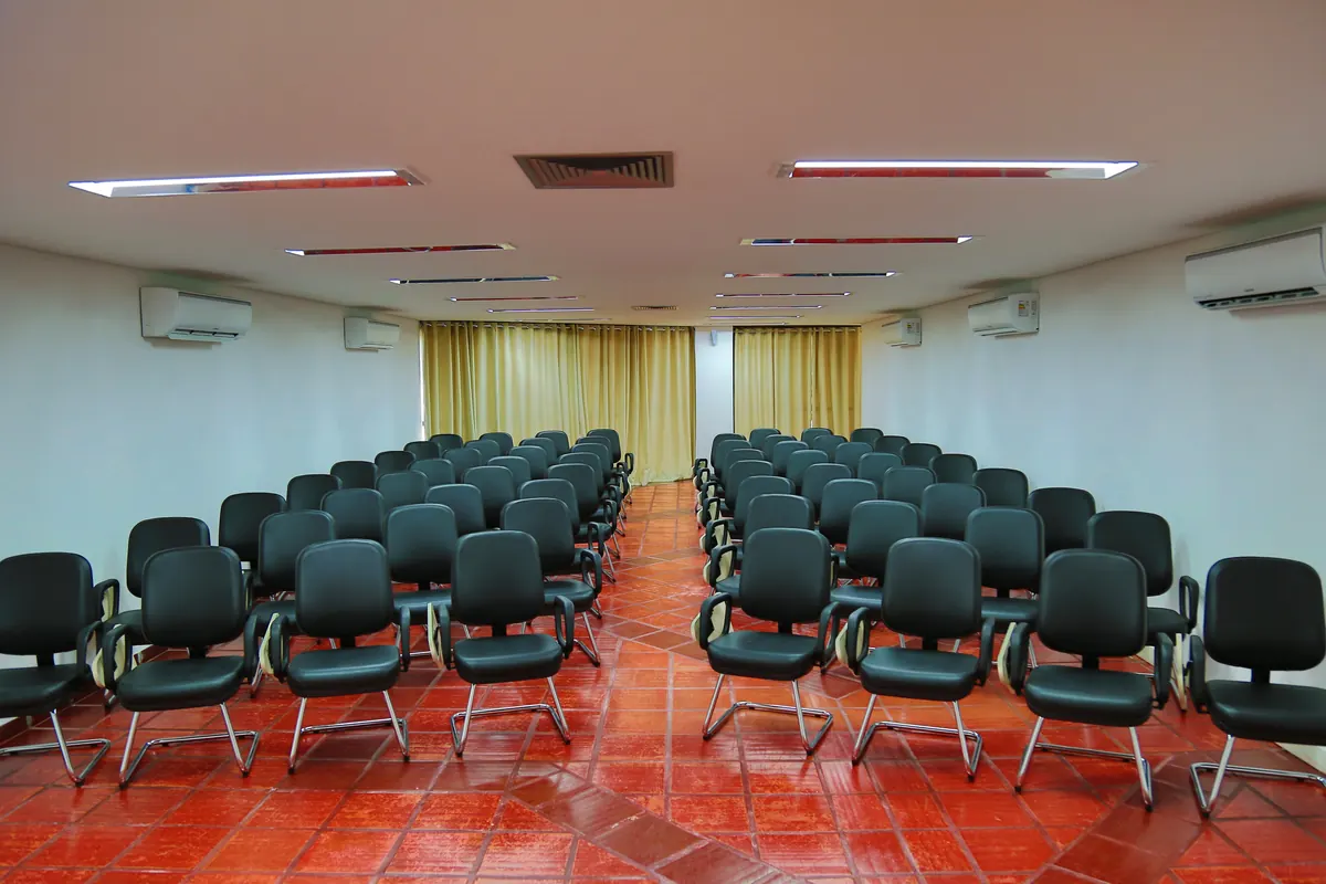 Sala de convenções com cadeiras estofadas em formato espinha de peixe, cortinas e ar-condicionado