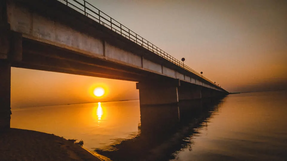 Sol se pondo sob a ponte sobre o rio Paraná, com o reflexo dourado na água